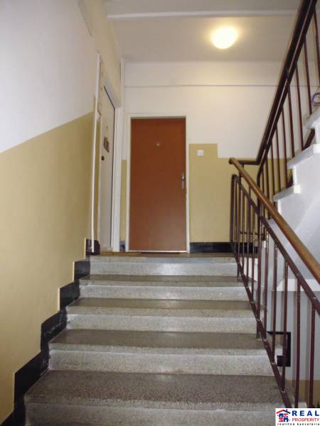 Staircase in an apartment building, brown railing, leads to the hallway of a one-bedroom apartment.