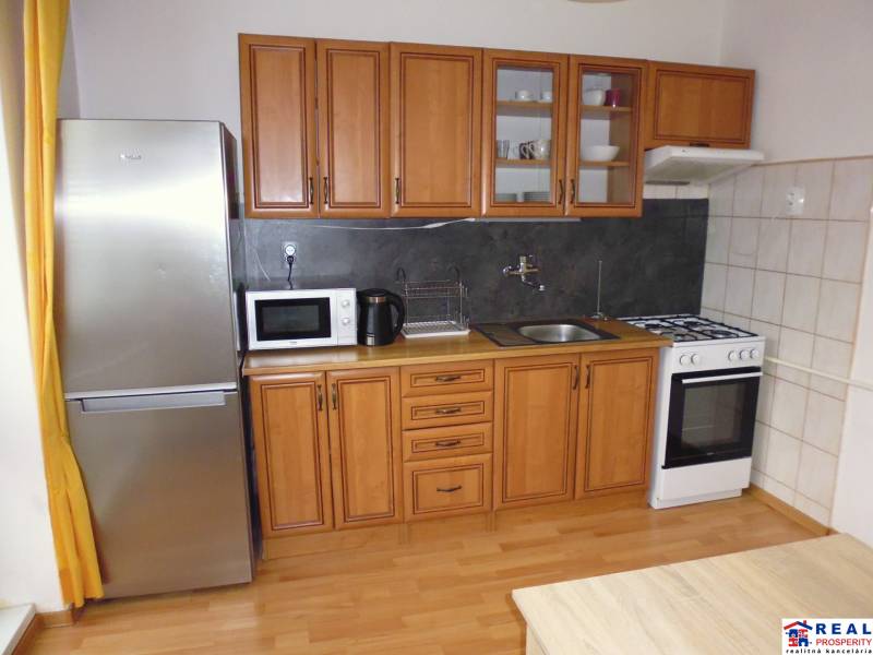 A kitchen in a studio apartment with a kitchen unit, wood-patterned flooring, and appliances.