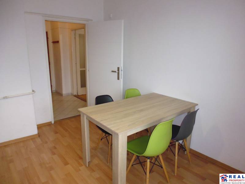 Dining area in a studio apartment with wood-patterned flooring and four chairs.