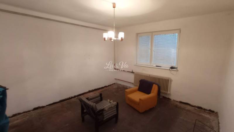 A room with a wooden floor decor, two armchairs, a window, and a radiator, family house.