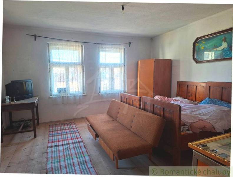 A room in a family house with wooden decor, a sofa, a TV, a bed, and a painting.