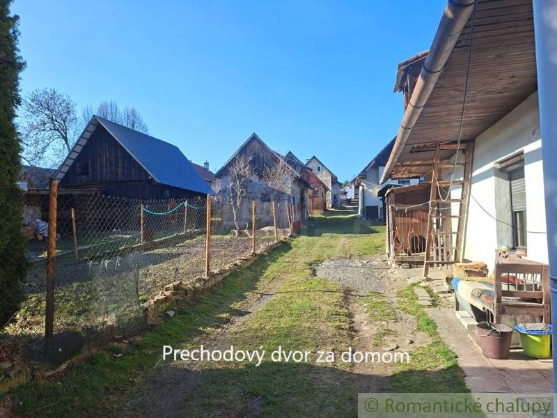 A transitional courtyard behind a family house in Východná, bordered by shelters and a fence.