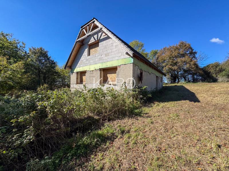 An unfinished building on agricultural and forest land in Lackov, surrounded by green trees and grass.