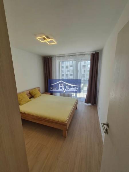 Bedroom with wood-patterned flooring in a 2-room apartment, double bed and curtains.