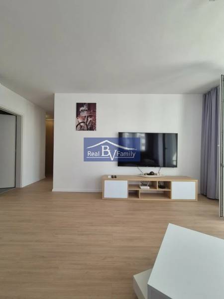 Living room of a two-room apartment with a wooden decor floor and a TV on the wall.