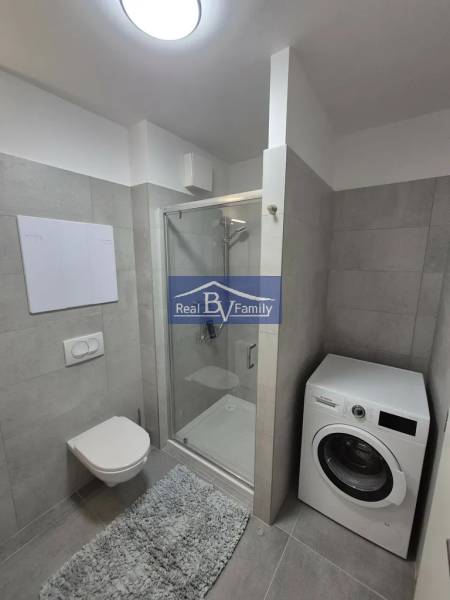 Bathroom with a shower and a washing machine in a 2-room apartment, tiles, neutral shades.