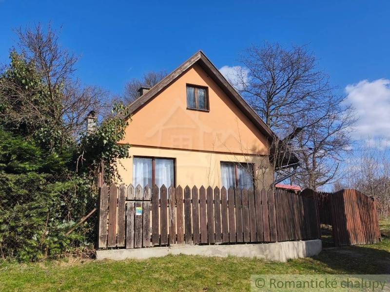 A cottage in Hronská Dúbrava surrounded by greenery and a wooden fence, with a clear blue sky.