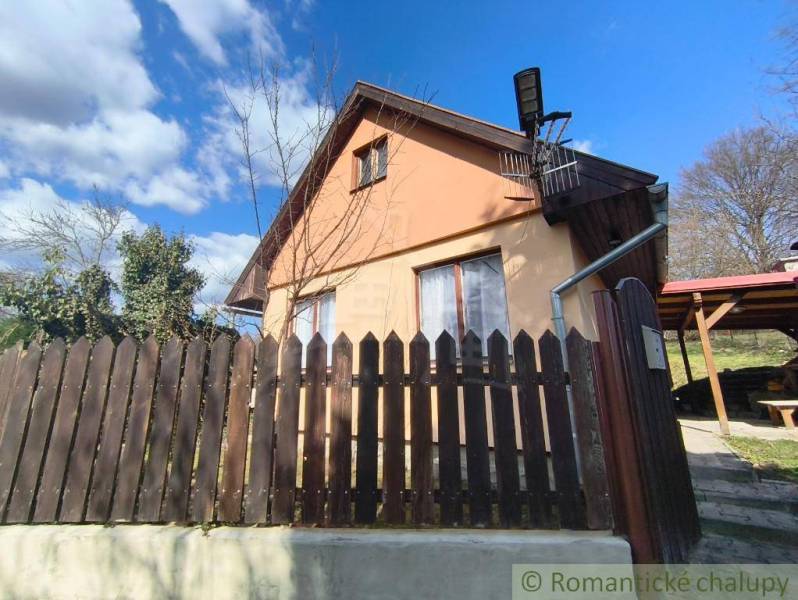 A cottage in Hronská Dúbrava with a wooden fence and a blue sky.