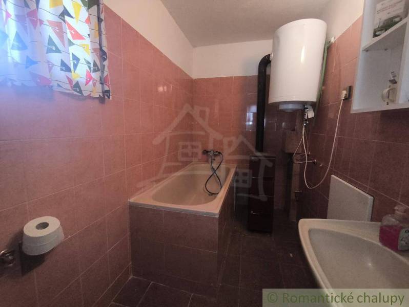 A bathroom in a cabin with a bathtub, sink, and electric boiler.