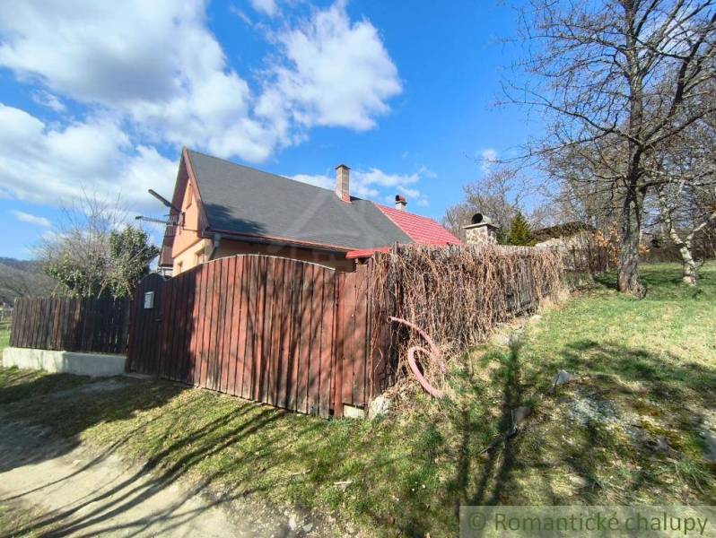 A cottage in Hronská Dúbrava with a garden, wooden fence, and blue sky.