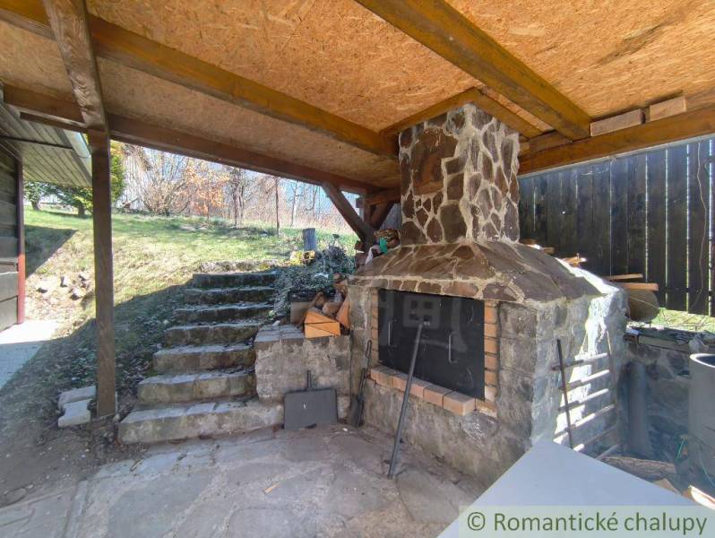 A covered outdoor fireplace with a stone chimney in a cabin in Hronská Dúbrava.