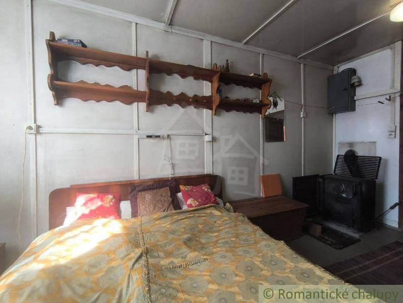 A bedroom in a cottage with simple furniture and a wood stove.