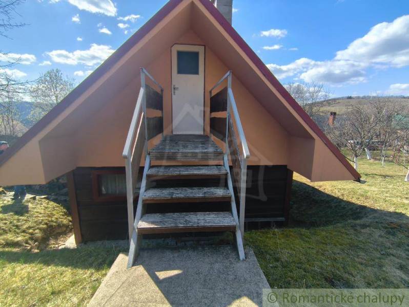 A cottage in Hronská Dúbrava with wooden stairs, surrounding trees, and a clear sky.