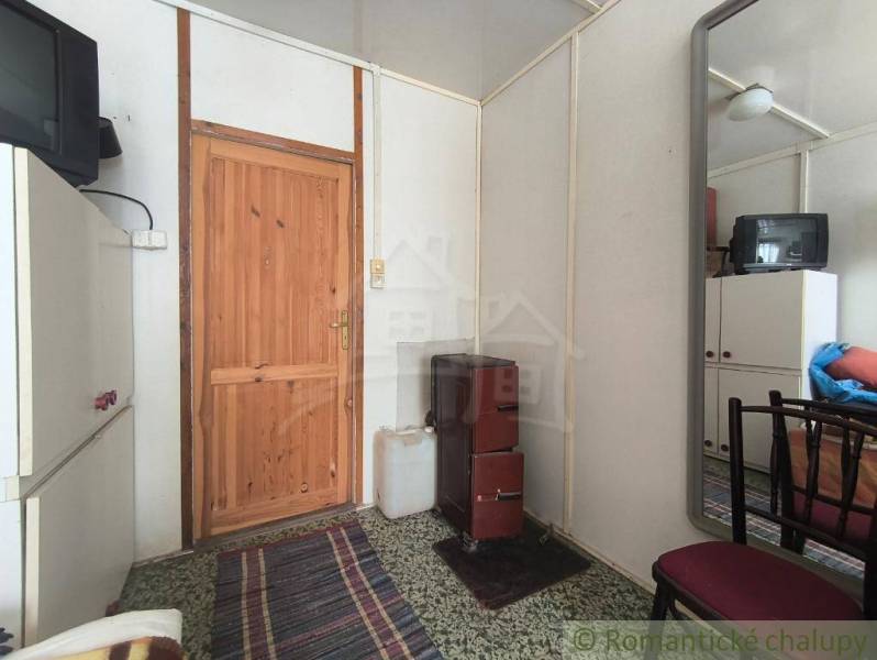 The interior of a cabin with wooden doors, an older television, and a stove on a floor with carpets.
