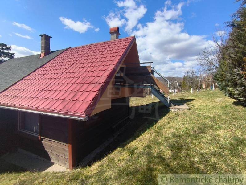 A cottage in Hronská Dúbrava with a staircase and a red roof on a vast meadow.