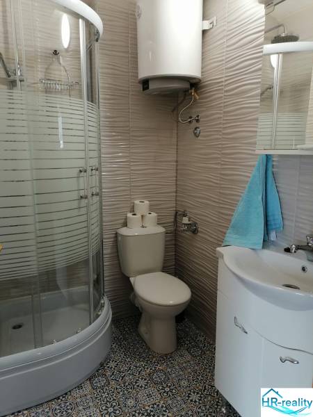 Bathroom in a holiday apartment with a toilet, shower, and patterned tiles.