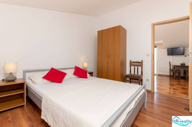Interior of a holiday apartment with a wood-patterned floor, a bed, and simple furniture.