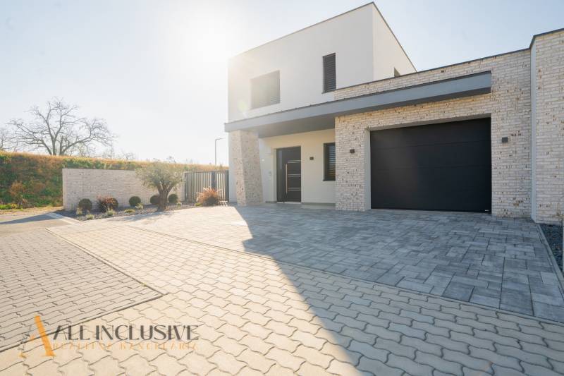 A family house in Gyor-Moson-Sopron with a garage and a paved courtyard, surrounded by greenery.