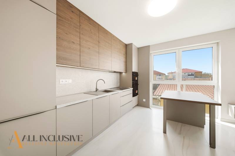 A kitchen in a 2-room apartment with a wooden decor floor and a large window.