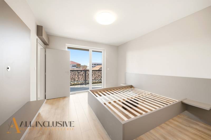 A bright bedroom with a bed and a balcony in a 2-room apartment, with a wooden decor floor.