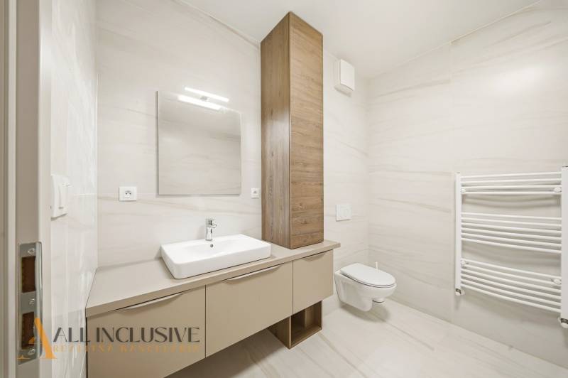 A bathroom in a 2-room apartment with a sink, mirror, and built-in toilet.