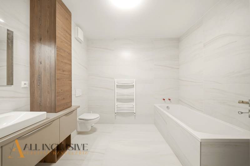 A bathroom with a bathtub and wooden decor in a 2-room apartment, simple lines and light walls.