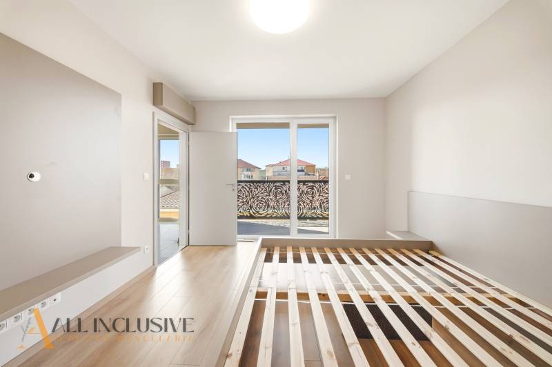 A bright bedroom with wood-patterned flooring and a view in a two-room apartment.