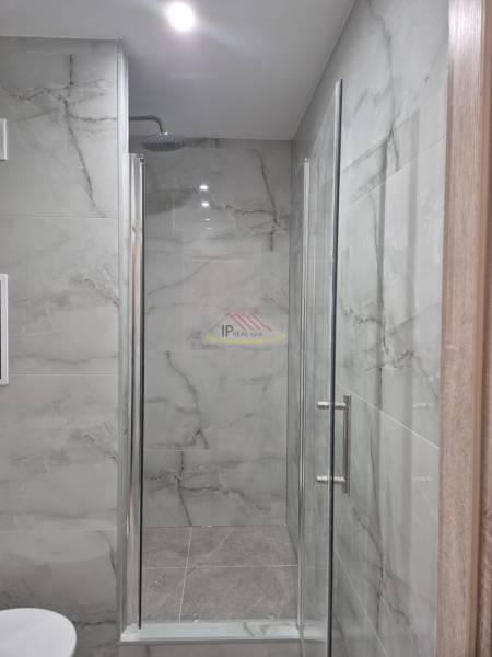A shower corner with glass doors and marble tiles in a studio apartment.