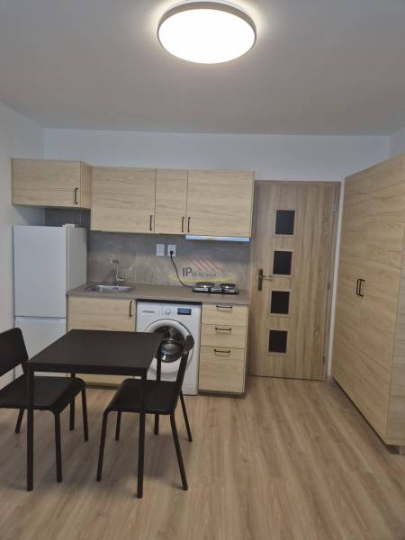 Kitchen unit in a studio apartment with a dining table and a floor with a wooden decor.