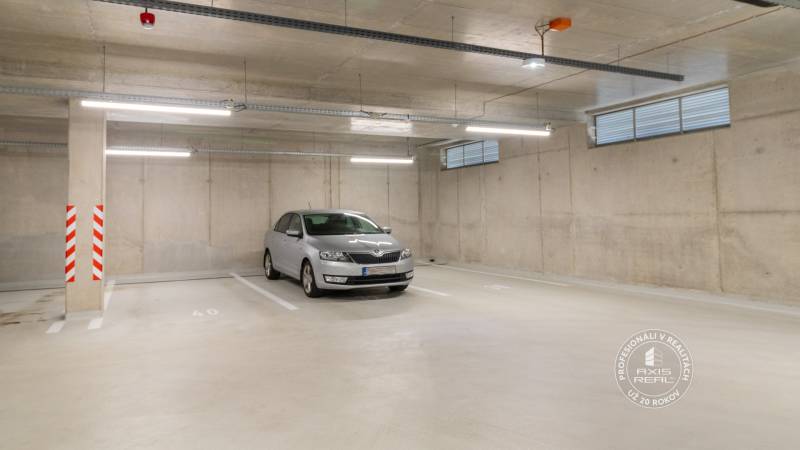Underground parking lot with a car, concrete walls, and lighting in the garages.