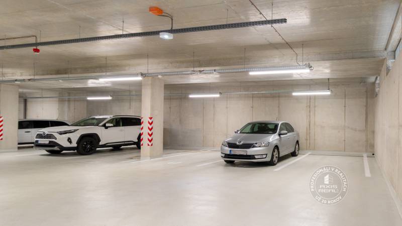 Underground parking spaces in a garage with two vehicles, concrete walls, and lighting.