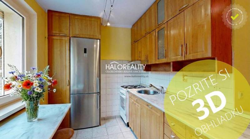 A kitchen with a light-colored unit and flowers, in a 2-room apartment, with a window and appliances.