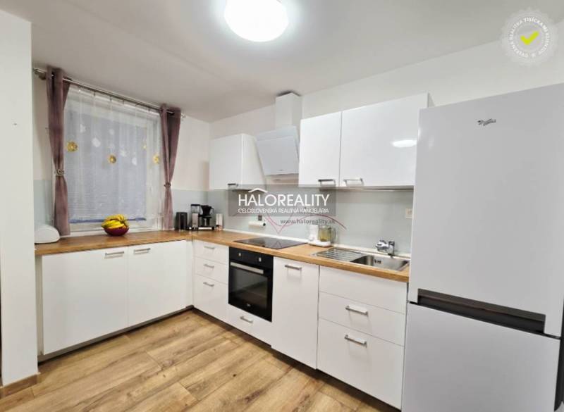 A kitchen with white cabinets, wood-patterned flooring, and modern appliances in a three-room apartment.
