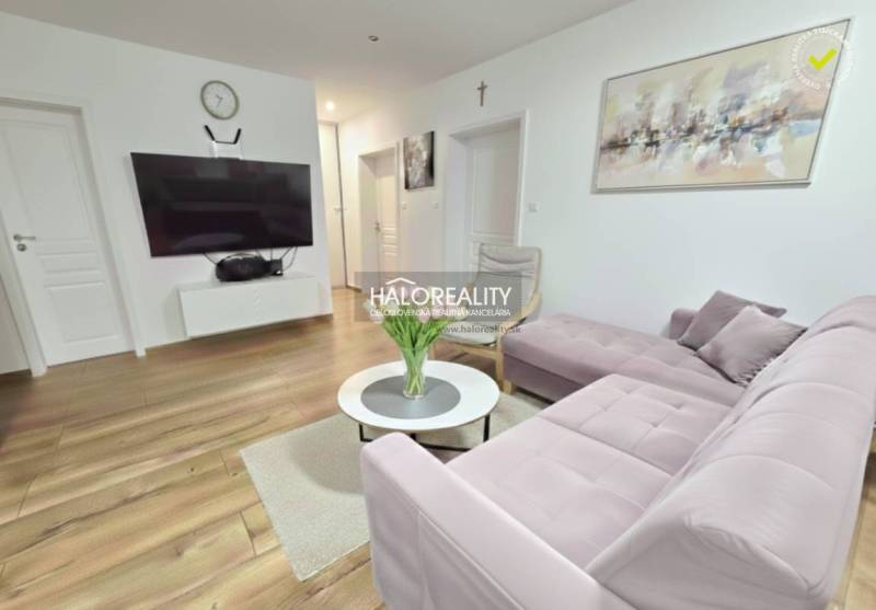 A kitchen and dining room in a three-room apartment with a wood-patterned floor and a pink sofa.