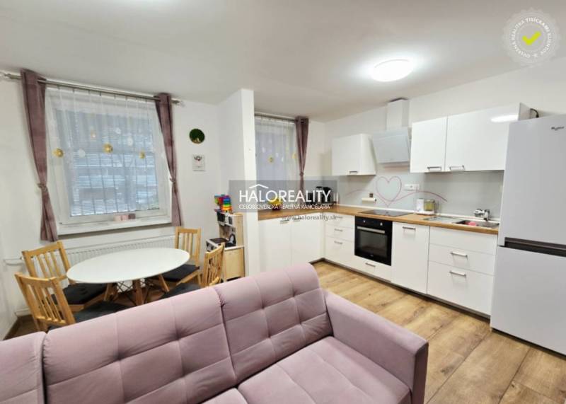 Living room with a pink sofa, kitchen, and wooden decor flooring in a three-room apartment.