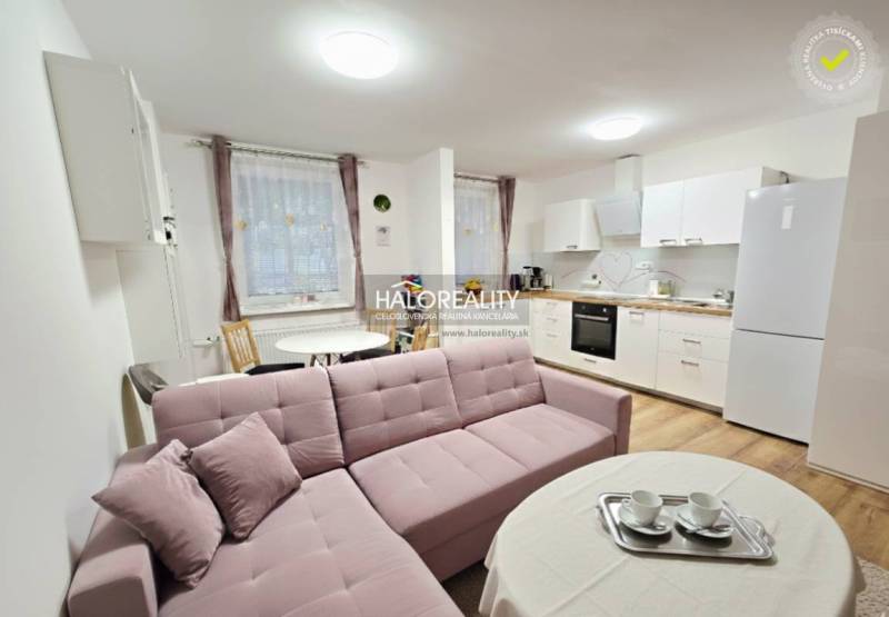 Living room in a three-room apartment with a corner sofa and kitchen, wooden decor flooring.