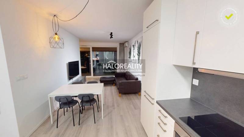 A kitchen in a 2-room apartment with white cabinets, a sofa, and plant decorations on the wall.