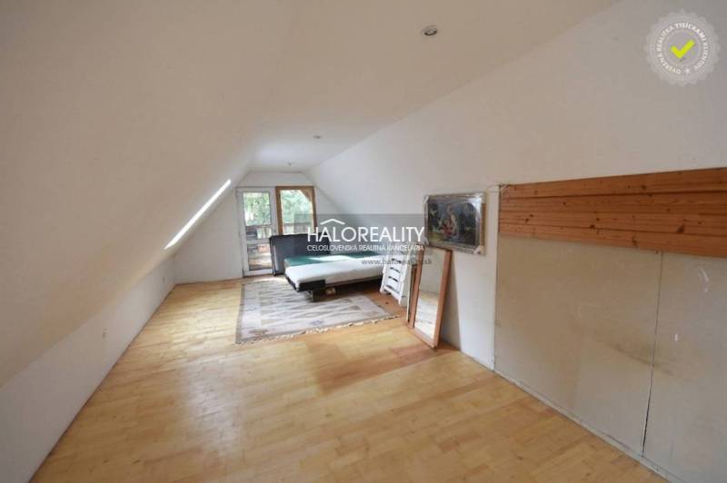 Attic room in a cottage with a bed, mirror, and floor with wooden decor.