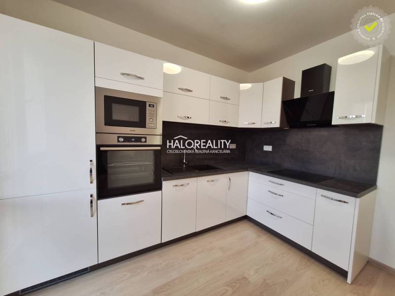 A kitchen with white cabinets, black appliances, and a wood-patterned floor in a three-room apartment.