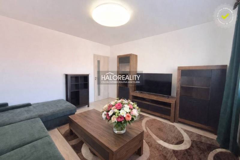 A living room with wood-patterned flooring, a TV, and flowers in a 3-room apartment.