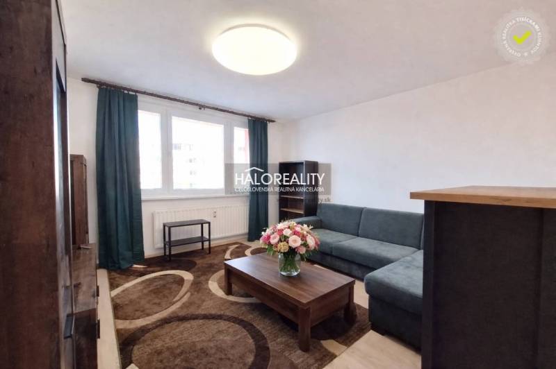 A living room with a sofa, carpet, and fresh flowers in a 3-room apartment.