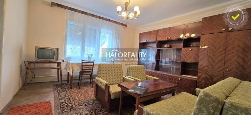 Living room in a family house with a wooden decor floor, a large couch, and shelves.