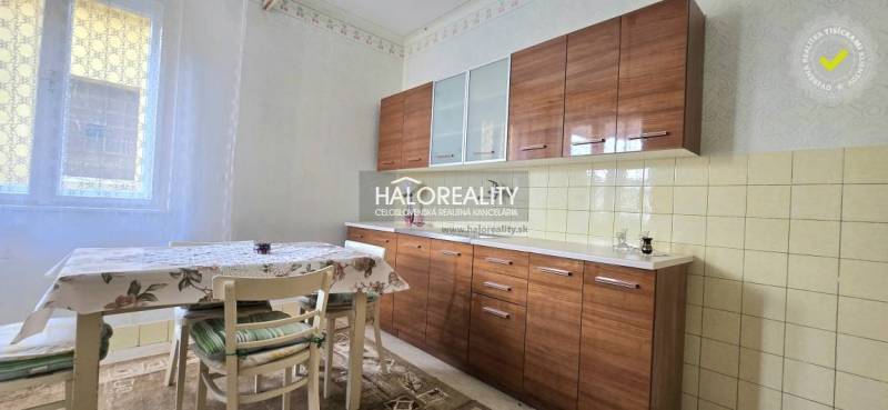 A kitchen in a family house, equipped with a dining table, chairs, and windows with white curtains.