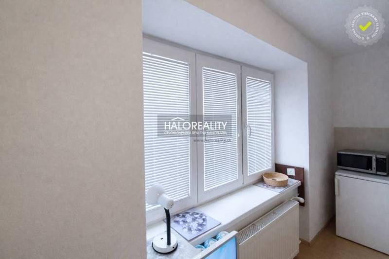 A studio apartment with white blinds and a microwave on a shelf.
