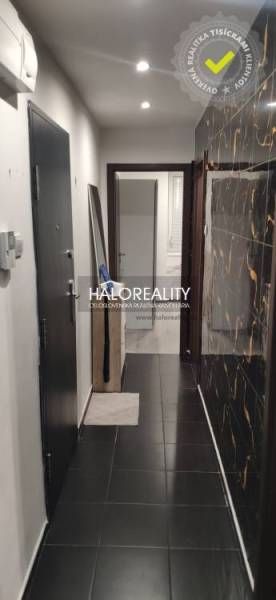 A narrow hallway with dark tiles in a 3-room apartment, the walls are adorned with black cladding.