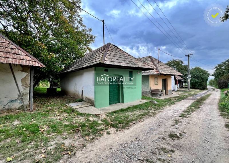 Traditional village houses and a road in the gardens of Mýtne Ludany, surrounded by trees.