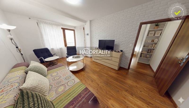 Living room with a sofa, TV, and wood-patterned flooring in a three-room apartment.
