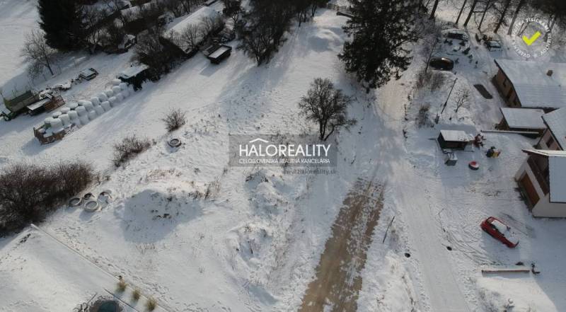 Snow-covered residential lands in Liptovské Beharovce surrounded by trees and buildings.