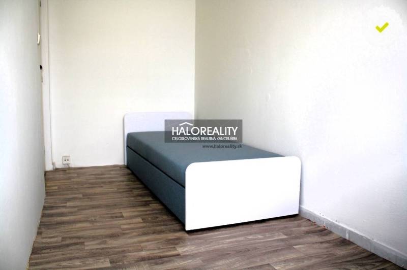 A single bed in a room, wood-patterned floor, white walls.