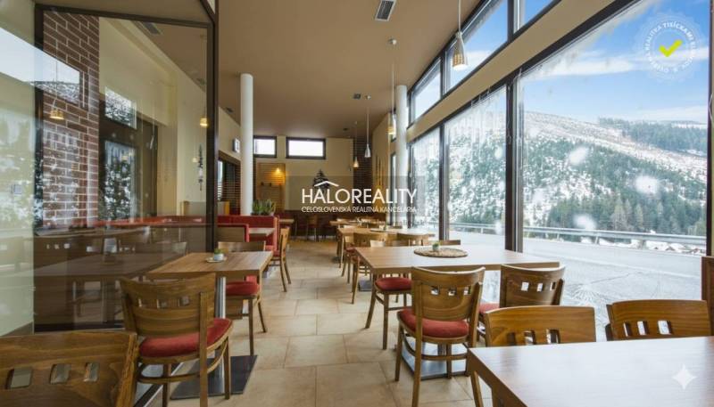 A hotel restaurant with a glass wall, overlooking snow-covered mountains and forests.